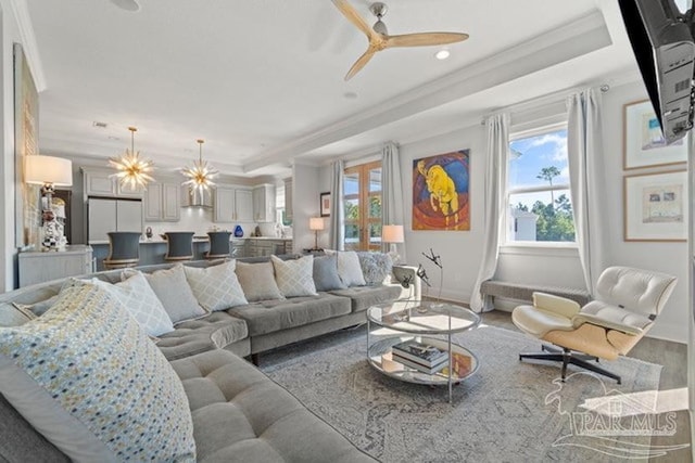 living room with a raised ceiling, crown molding, plenty of natural light, and ceiling fan with notable chandelier