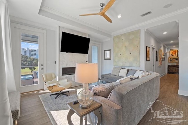 living room featuring a high end fireplace, wood-type flooring, ceiling fan, and crown molding