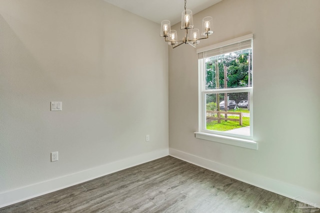 unfurnished room featuring a wealth of natural light, wood-type flooring, and an inviting chandelier