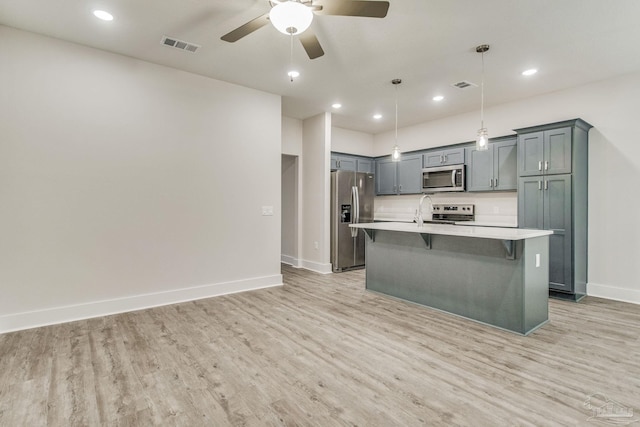 kitchen featuring stainless steel appliances, an island with sink, pendant lighting, light hardwood / wood-style floors, and a breakfast bar