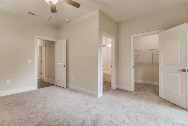 unfurnished bedroom with carpet, a walk in closet, ensuite bath, ceiling fan, and a closet