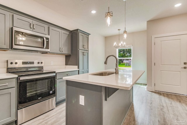 kitchen with a center island with sink, hanging light fixtures, sink, light wood-type flooring, and appliances with stainless steel finishes