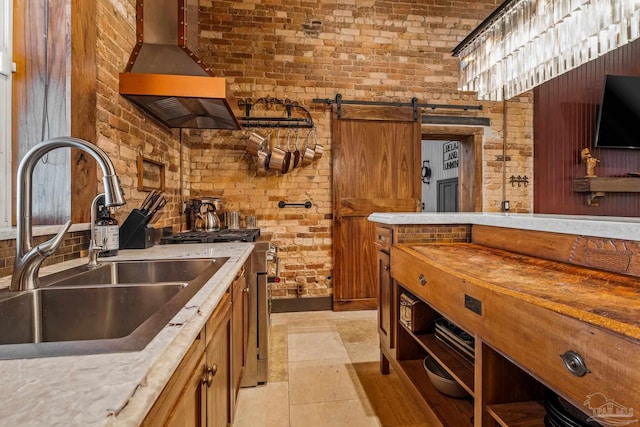 kitchen with sink, wall chimney exhaust hood, high end stainless steel range oven, a barn door, and brick wall