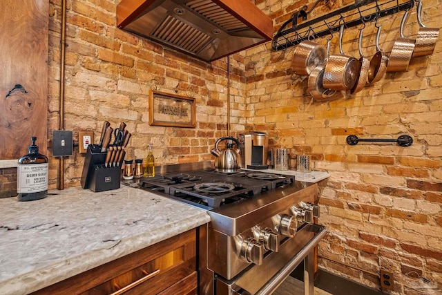 kitchen with high end stainless steel range oven, light stone counters, premium range hood, and brick wall