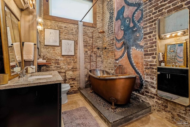 bathroom featuring a washtub, vanity, toilet, and brick wall