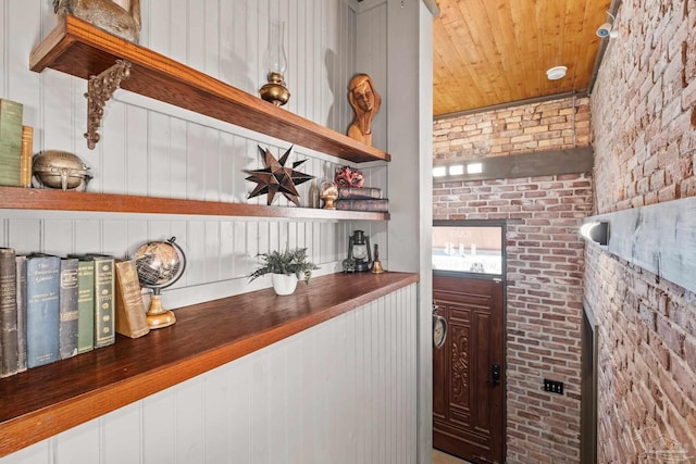 bar featuring wood walls, wooden ceiling, and brick wall