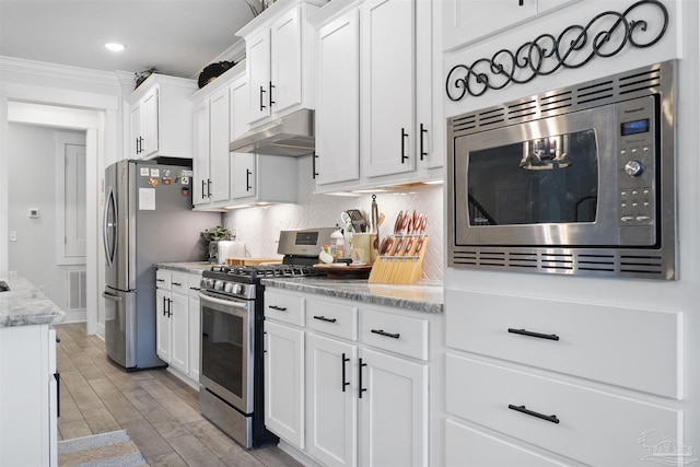 kitchen with white cabinetry, crown molding, stainless steel appliances, light stone countertops, and decorative backsplash