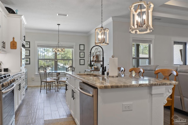 kitchen with an inviting chandelier, appliances with stainless steel finishes, pendant lighting, a kitchen island with sink, and white cabinets