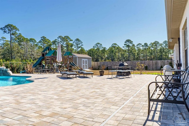 view of patio featuring a fenced in pool, pool water feature, a playground, and a storage unit