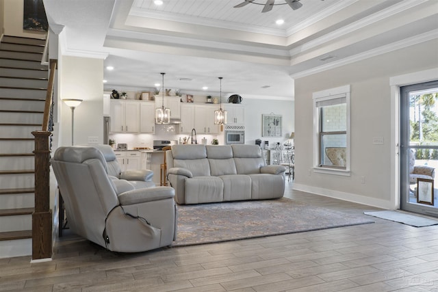 living room featuring a raised ceiling, crown molding, ceiling fan, and light wood-type flooring