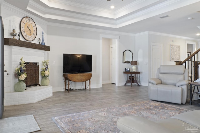 living room with a raised ceiling, ornamental molding, and light hardwood / wood-style flooring