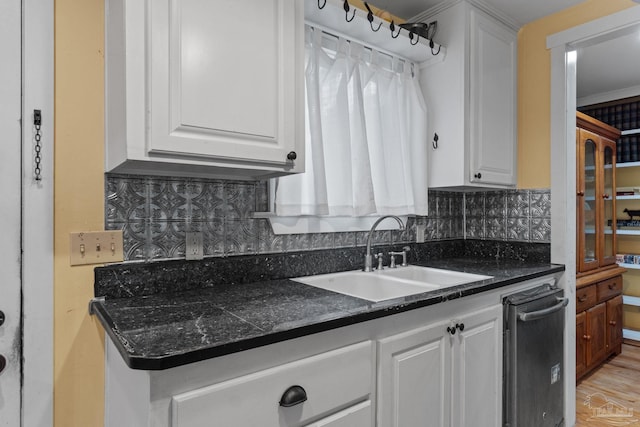 kitchen with a sink, light wood-style floors, white cabinets, tasteful backsplash, and dark countertops