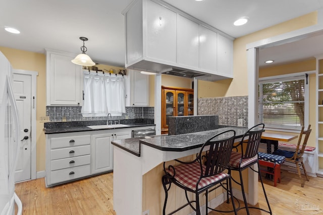 kitchen with white cabinets, dark countertops, a breakfast bar, light wood-style floors, and a sink