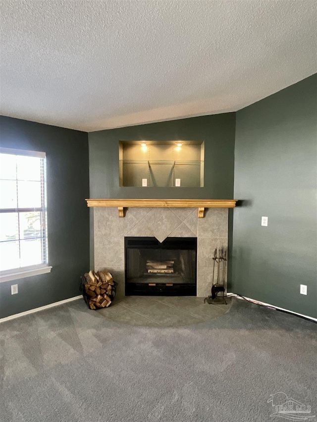 unfurnished living room featuring a textured ceiling, carpet, a tile fireplace, and baseboards