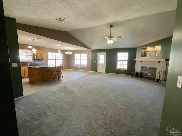 unfurnished living room featuring lofted ceiling, a tiled fireplace, visible vents, and light colored carpet