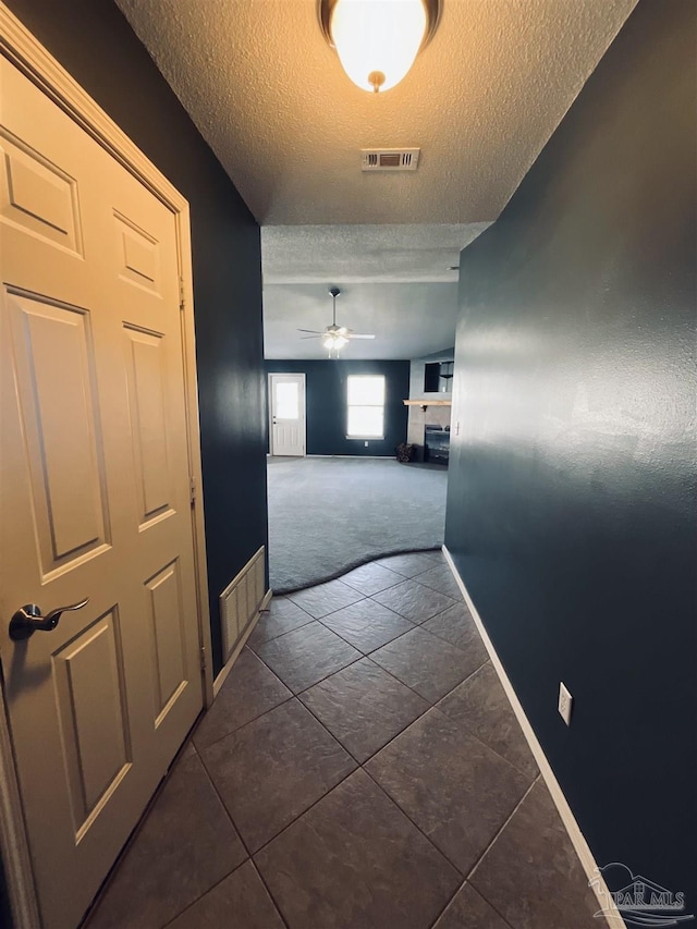 hallway featuring a textured ceiling, visible vents, and baseboards