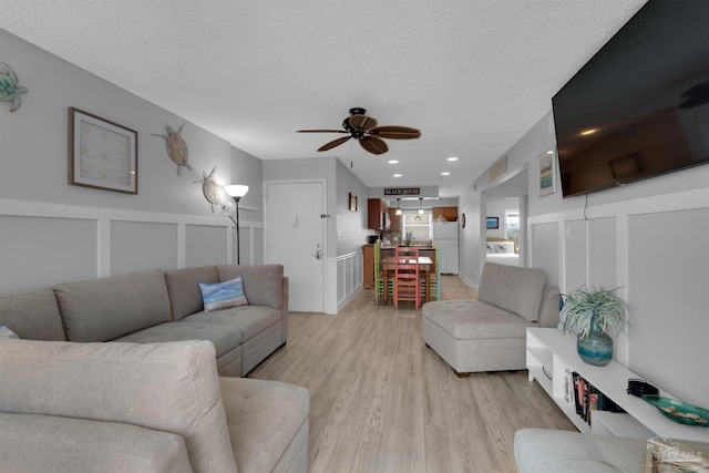 living area with a textured ceiling, a decorative wall, a wainscoted wall, a ceiling fan, and light wood-style floors