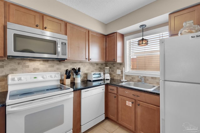 kitchen featuring dark countertops, backsplash, brown cabinetry, a sink, and white appliances