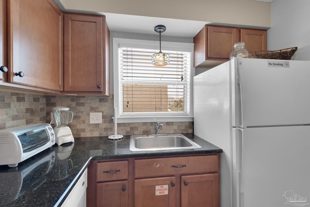 kitchen featuring dark countertops, brown cabinetry, a sink, and freestanding refrigerator