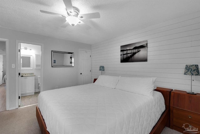 bedroom featuring a textured ceiling, ceiling fan, light carpet, and ensuite bath