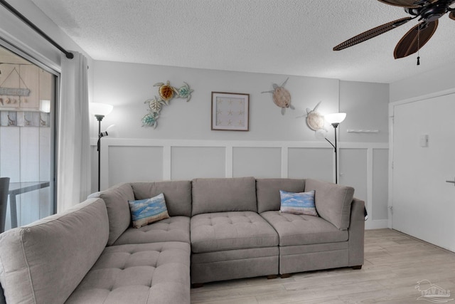 living room with a textured ceiling, light wood-type flooring, a wealth of natural light, and a decorative wall