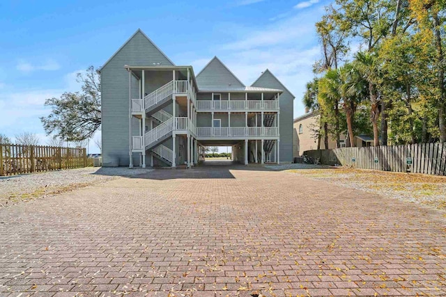 rear view of property featuring a carport, stairway, decorative driveway, and fence