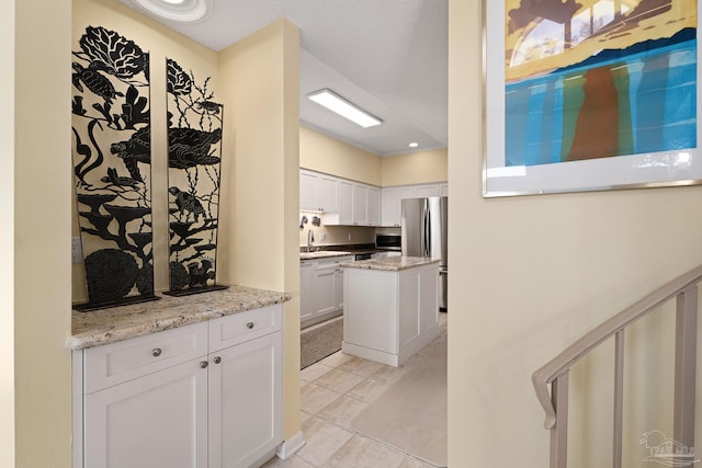 kitchen featuring light stone countertops, a kitchen island, a sink, white cabinets, and appliances with stainless steel finishes