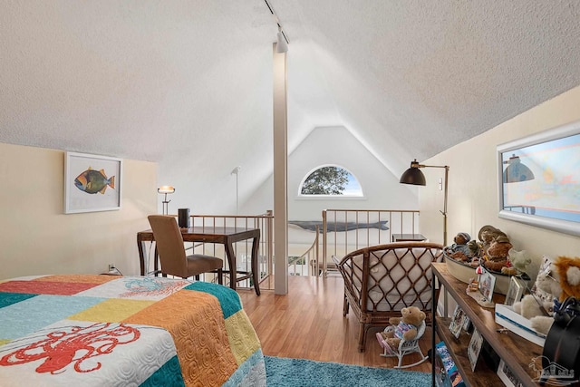 bedroom featuring vaulted ceiling, rail lighting, wood finished floors, and a textured ceiling