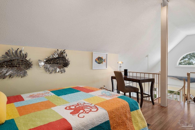 bedroom with vaulted ceiling, wood finished floors, and a textured ceiling