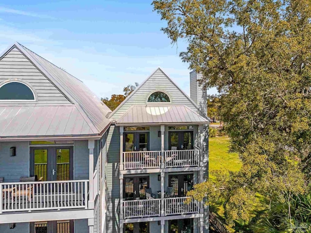 view of front facade with a standing seam roof, french doors, metal roof, a balcony, and a chimney