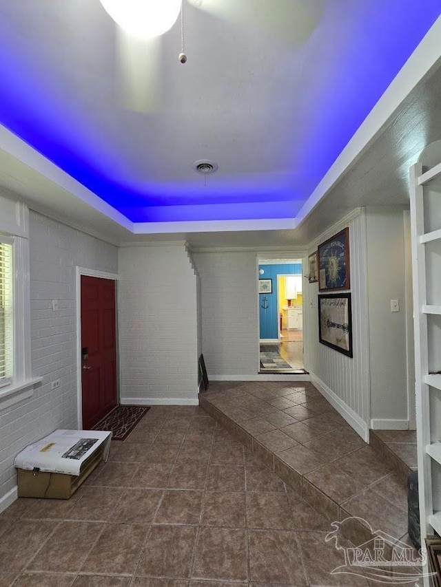 interior space featuring dark tile patterned flooring, a raised ceiling, and brick wall