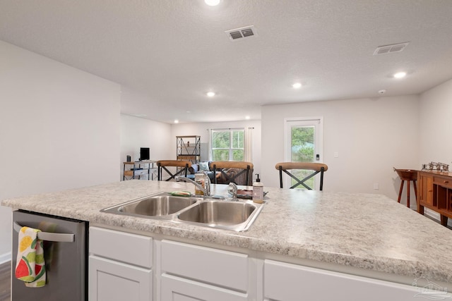 kitchen featuring white cabinetry, sink, stainless steel dishwasher, a textured ceiling, and a kitchen island with sink