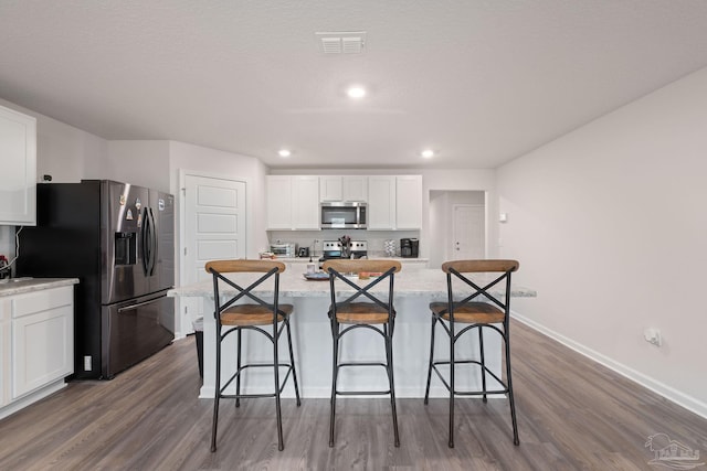 kitchen featuring light stone counters, stainless steel appliances, hardwood / wood-style flooring, white cabinetry, and an island with sink