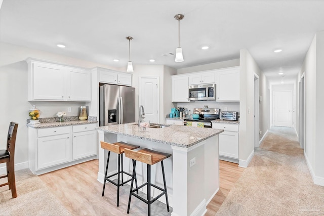 kitchen featuring stainless steel appliances, a sink, light wood-style floors, a center island with sink, and white cabinetry