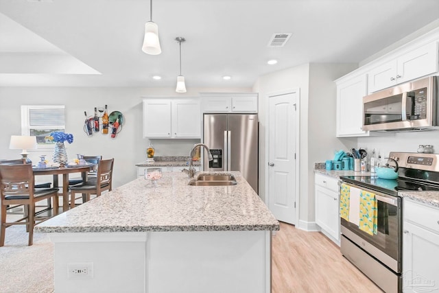 kitchen with stainless steel appliances, a sink, white cabinetry, an island with sink, and light stone countertops