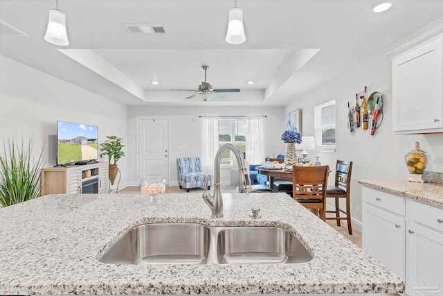 kitchen featuring a sink, baseboards, a tray ceiling, light stone counters, and hanging light fixtures