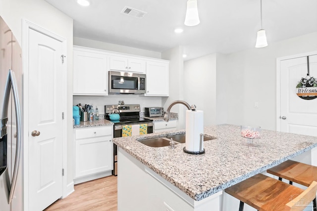 kitchen featuring appliances with stainless steel finishes, a sink, white cabinetry, light wood-style floors, and light stone countertops