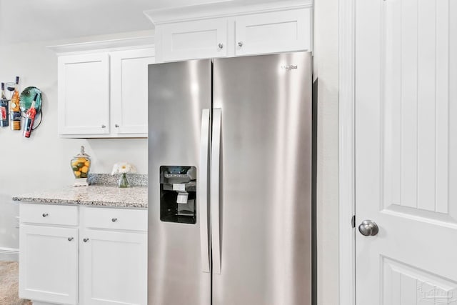 kitchen with stainless steel refrigerator with ice dispenser, light stone countertops, and white cabinetry