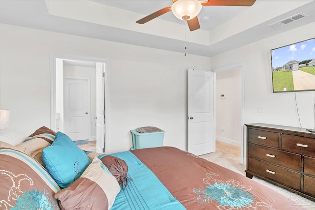 bedroom featuring a raised ceiling, light colored carpet, baseboards, connected bathroom, and ceiling fan