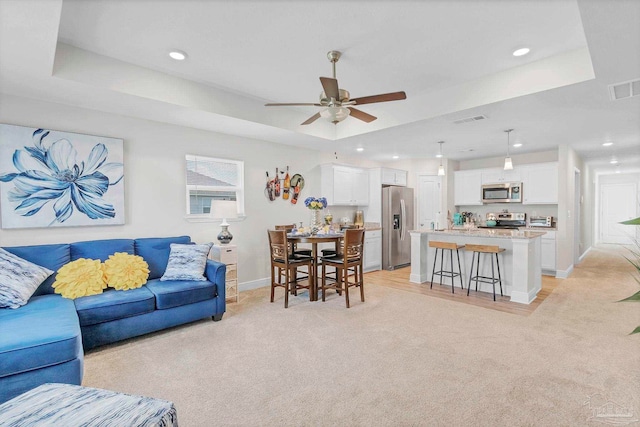 living area with light colored carpet, recessed lighting, baseboards, a ceiling fan, and a tray ceiling