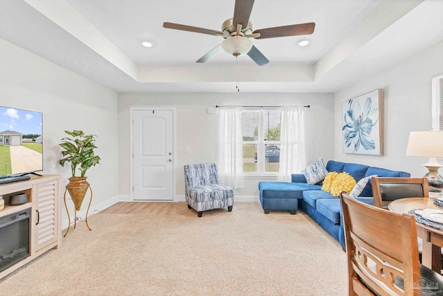 living area with a tray ceiling, light carpet, a ceiling fan, baseboards, and recessed lighting
