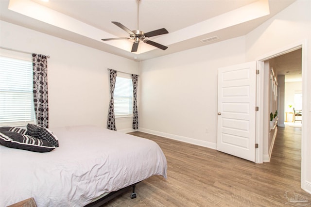 bedroom with hardwood / wood-style floors, ceiling fan, and a raised ceiling