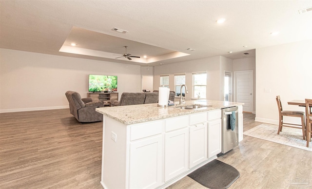 kitchen with a center island with sink, sink, a tray ceiling, light hardwood / wood-style flooring, and white cabinets