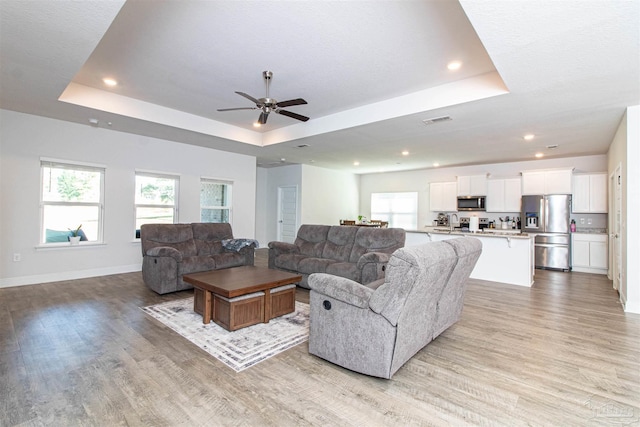 living room with light hardwood / wood-style flooring, ceiling fan, and a raised ceiling