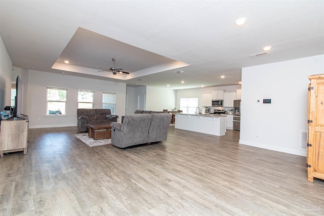 living room featuring light hardwood / wood-style floors, ceiling fan, a raised ceiling, and sink