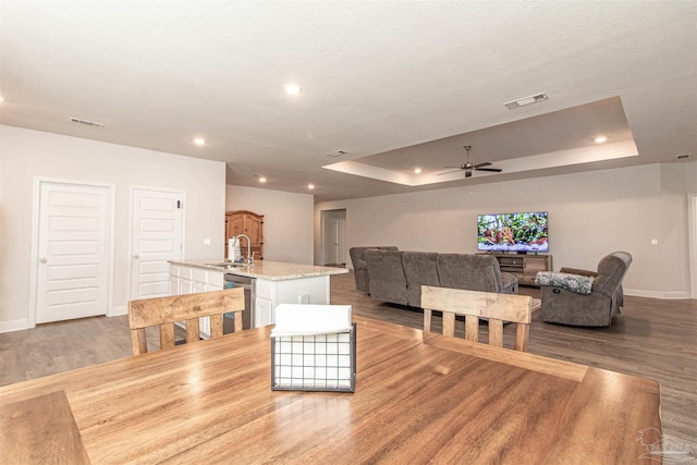 dining area with a tray ceiling, sink, ceiling fan, and light hardwood / wood-style flooring