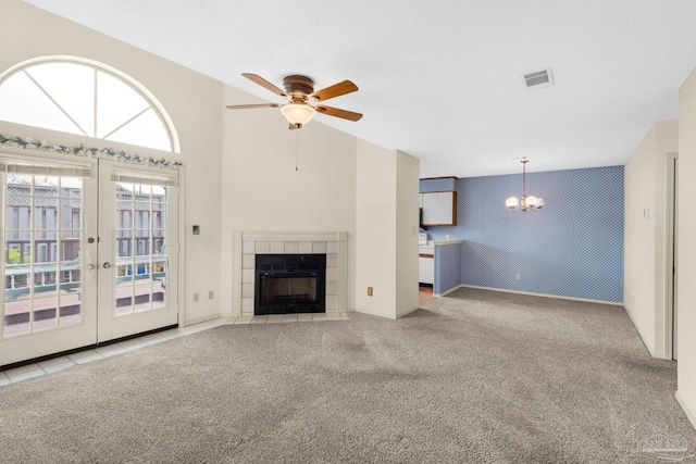 unfurnished living room with ceiling fan with notable chandelier, light carpet, a tile fireplace, and french doors