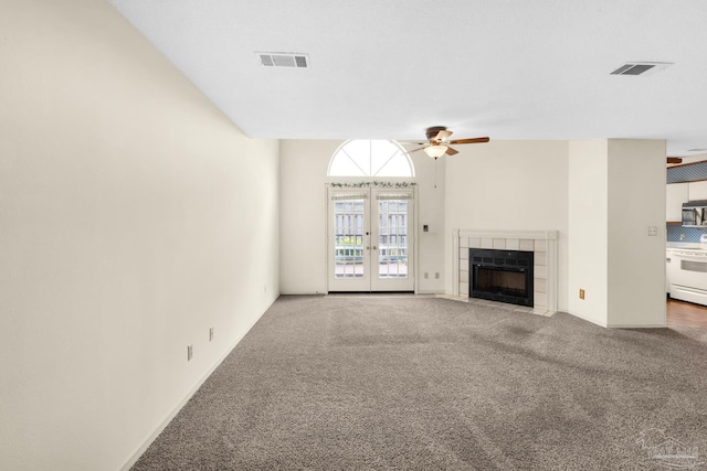 unfurnished living room featuring french doors, carpet floors, ceiling fan, and a tiled fireplace