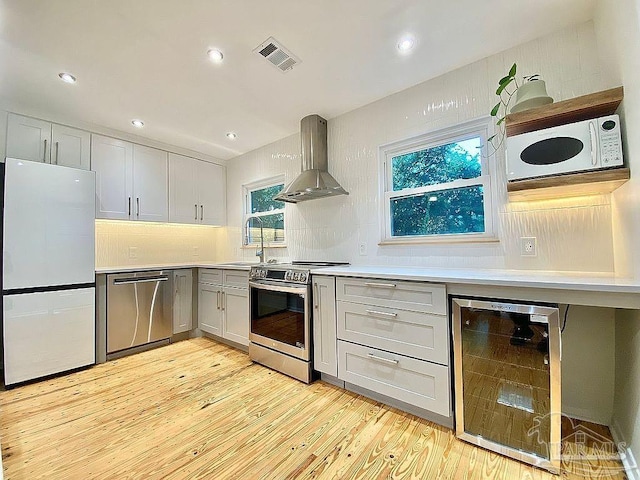 kitchen with light hardwood / wood-style floors, tasteful backsplash, wall chimney exhaust hood, stainless steel appliances, and beverage cooler