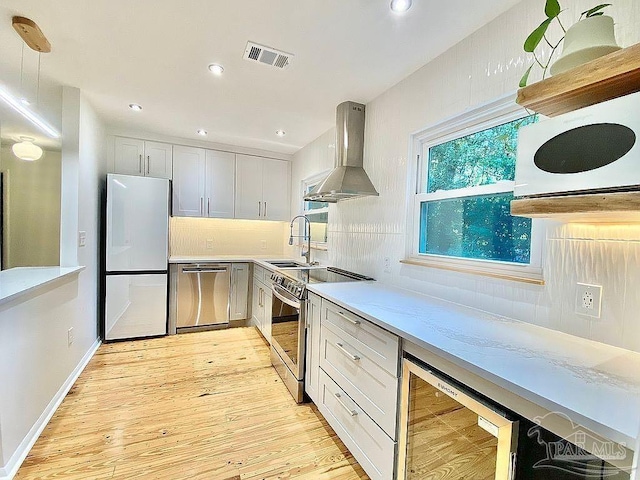 kitchen with appliances with stainless steel finishes, white cabinets, wall chimney exhaust hood, beverage cooler, and sink